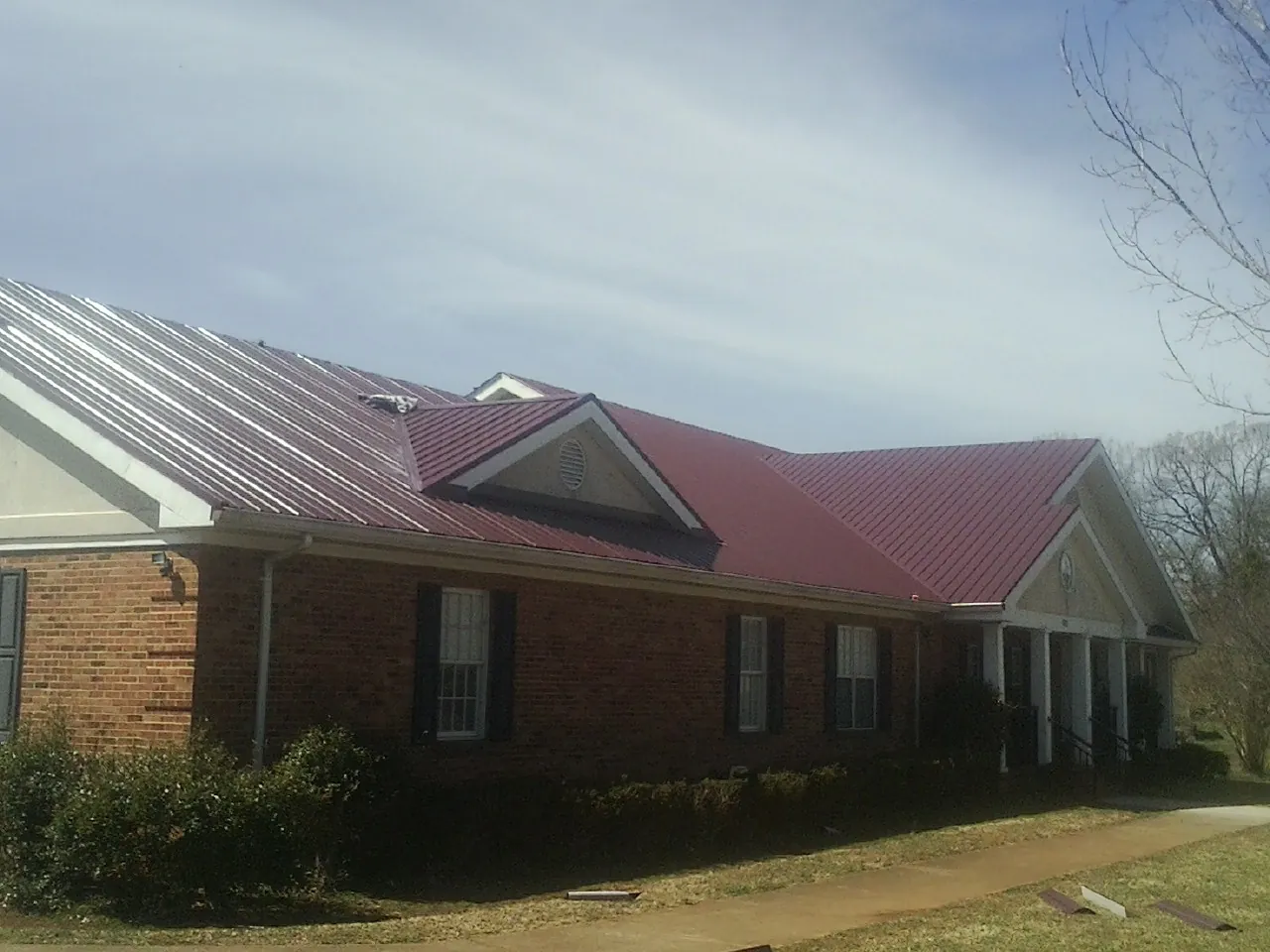 Red metal roof with gabled entries on a long brick building, from a Hail Damage Roof Repair job in Clover