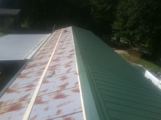 Old rusted panels beside newly installed green metal roofing — Wind Damage Roof Repair by Roofing Brothers in Clover