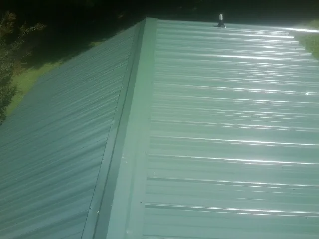 New green metal panels meeting at the ridge of a roof — Flat Roof Repair work by our crew in Clover