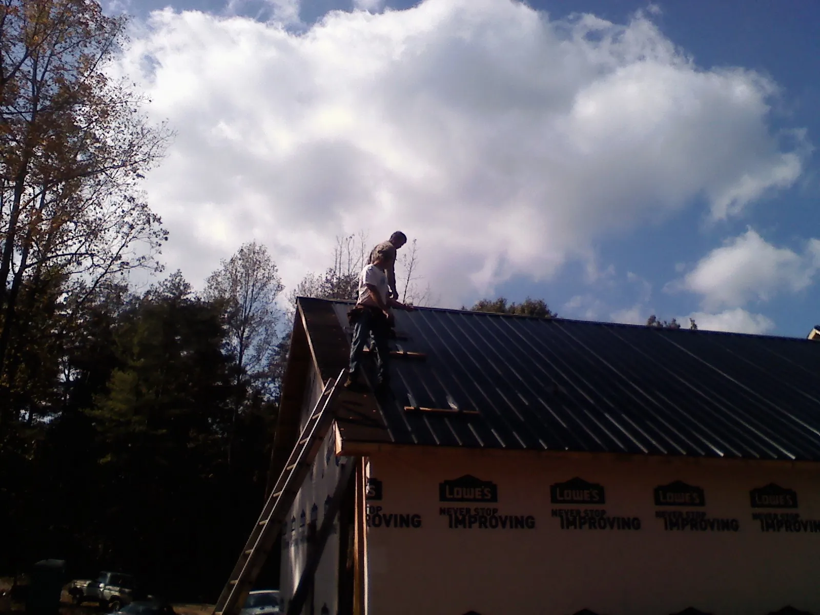 Roofer fastening dark metal panels high against a cloudy sky, from a Roof Inspection job in Clover