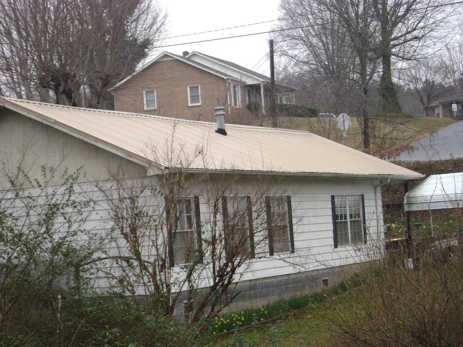 Tan metal roof on a white sided house set into a hillside — Commercial Roofing by Roofing Brothers in Clover